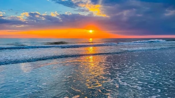 Ein Sonnenuntergang über dem Meer, wobei Wellen den Himmel spiegeln.