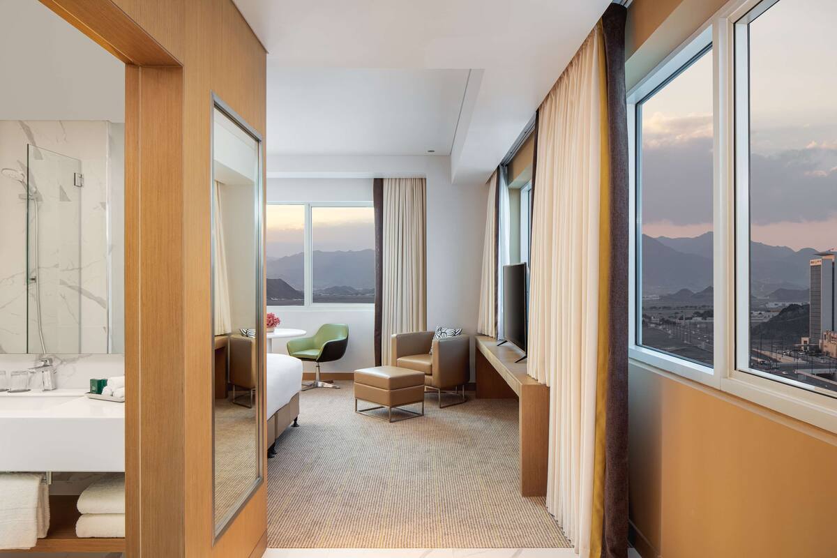 Une chambre d’hôtel avec une grande fenêtre, un lit, un bureau et une chaise.