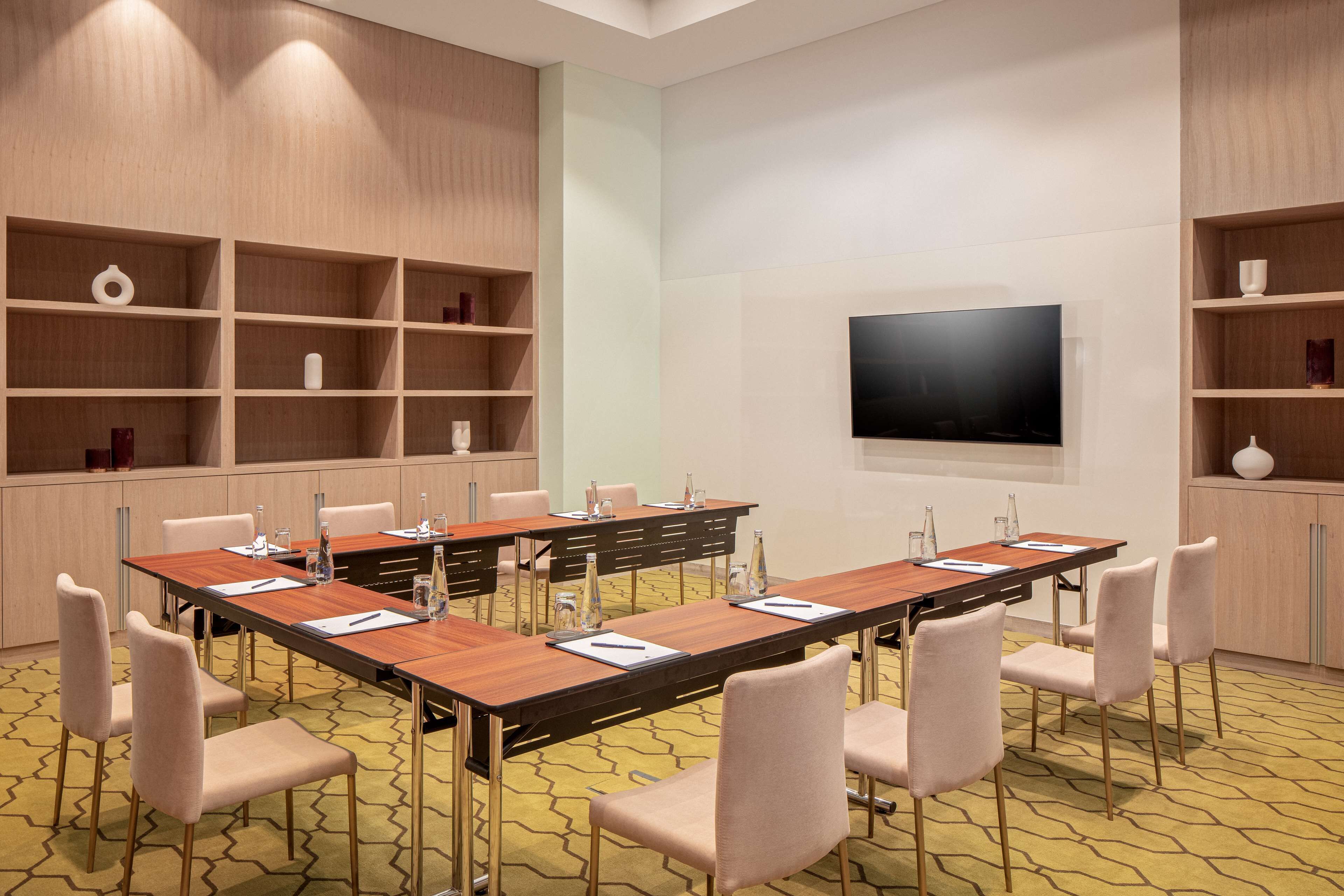 Een vergaderzaal met een lange tafel, stoelen, een televisie en planken met diverse spullen.