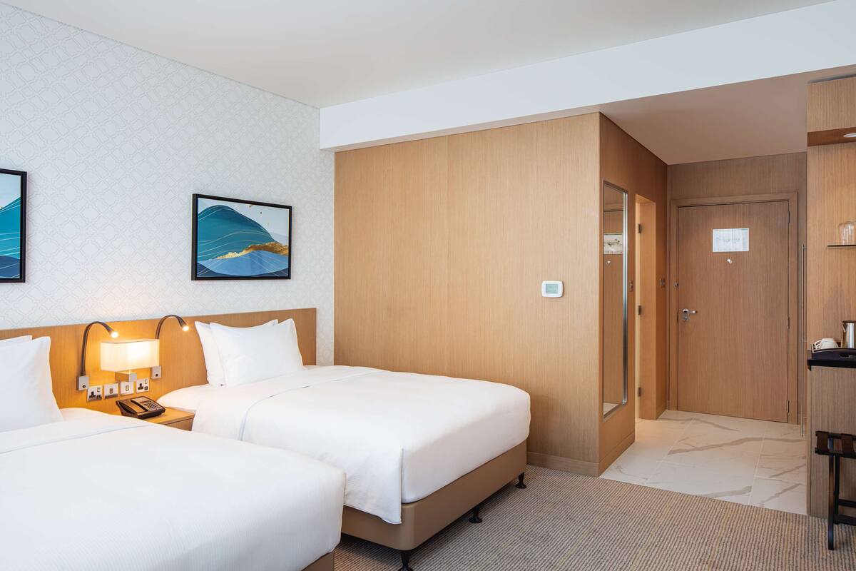 Une chambre d’hôtel avec deux lits, une armoire en bois, un bureau avec une lampe et un téléphone fixé au mur.