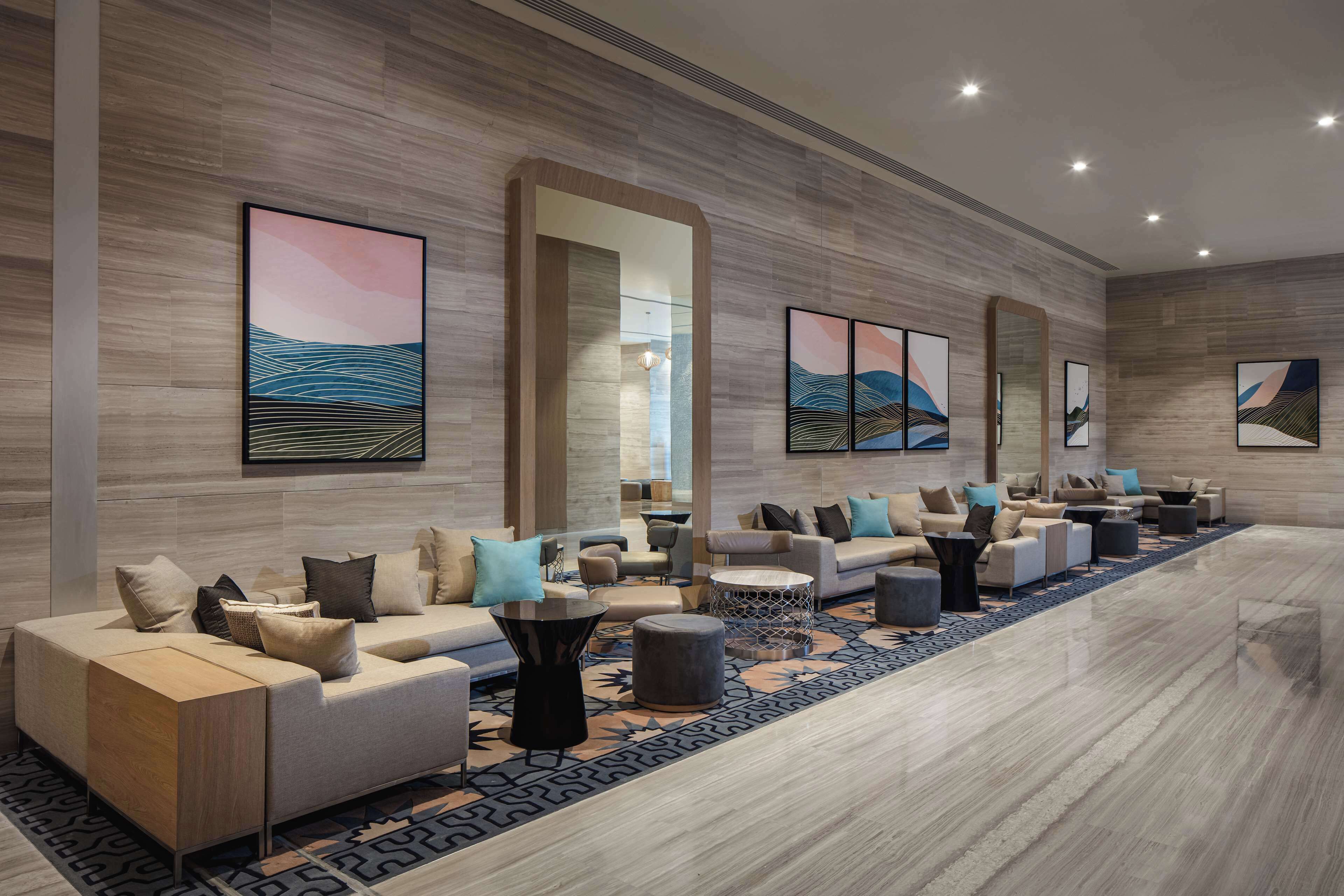 Um lobby de hotel moderno com um balcão de recepção extenso, diversas áreas de estar e uma grande obra de arte abstrata na parede.