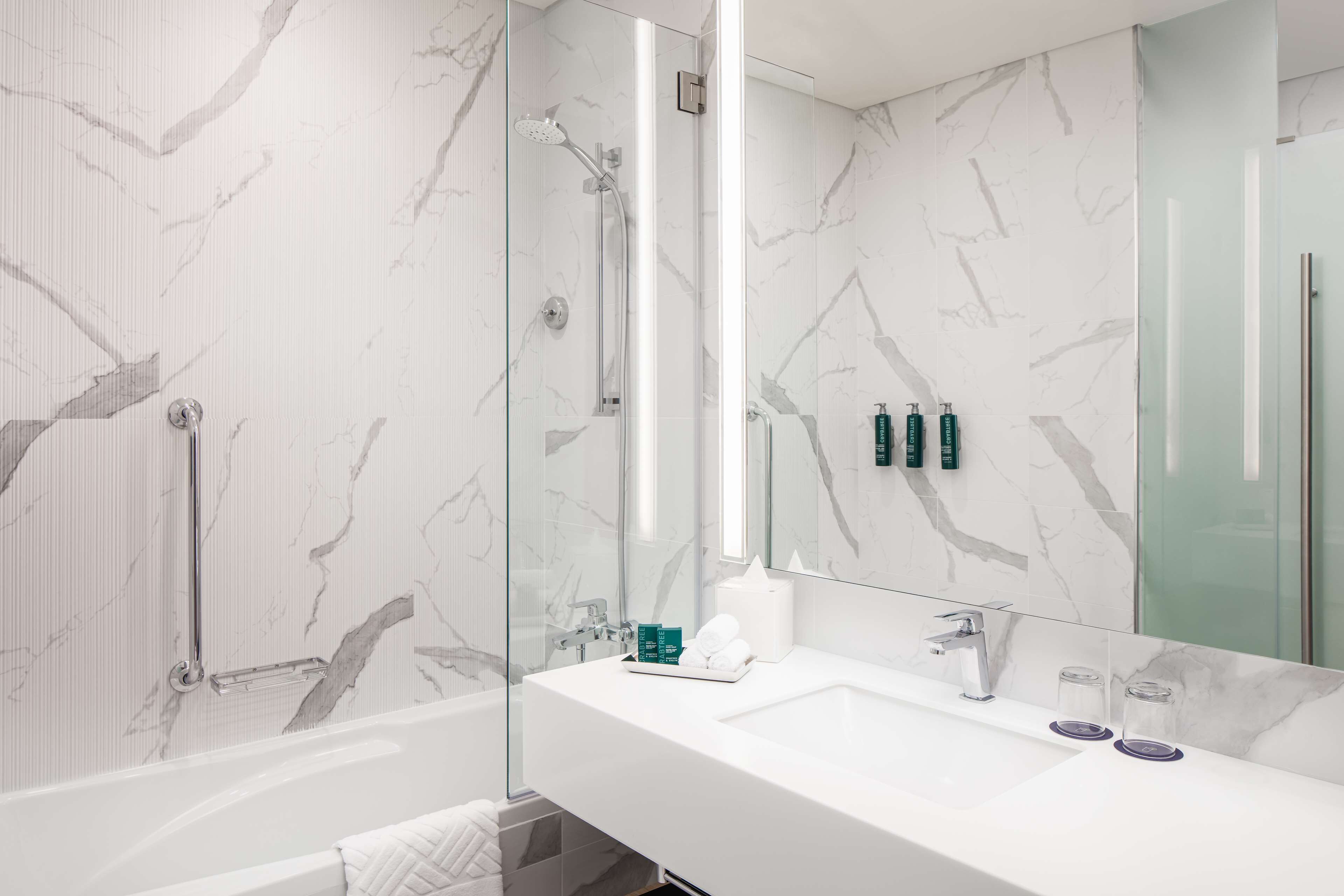 A modern bathroom with a glass-enclosed shower, a white sink with a large mirror, and marble-patterned walls.