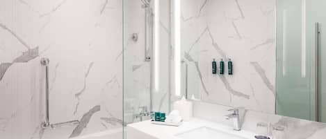 A modern bathroom with a glass-enclosed shower, a white sink with a large mirror, and marble-patterned walls.