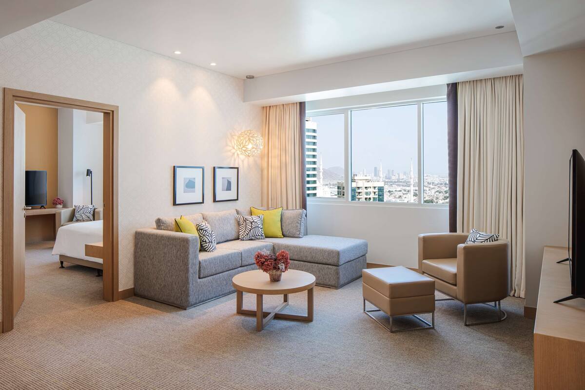 Une chambre d’hôtel moderne dotée d’une grande fenêtre, d’un canapé, d’une table basse, d’un téléviseur et d’un bureau.