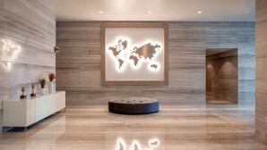 Een moderne lobby met een wereldkaart muurschildering, een witte consoles en decoratieve items, en een ronde poef.