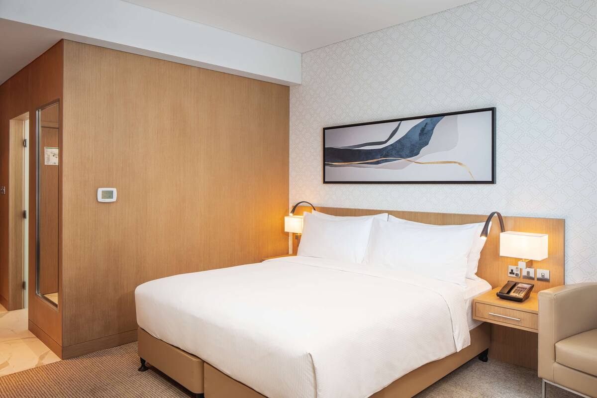 Une chambre d’hôtel avec un grand lit, des lampes de chevet, une table de chevet, une chaise et un tableau abstrait encadré accroché au mur.