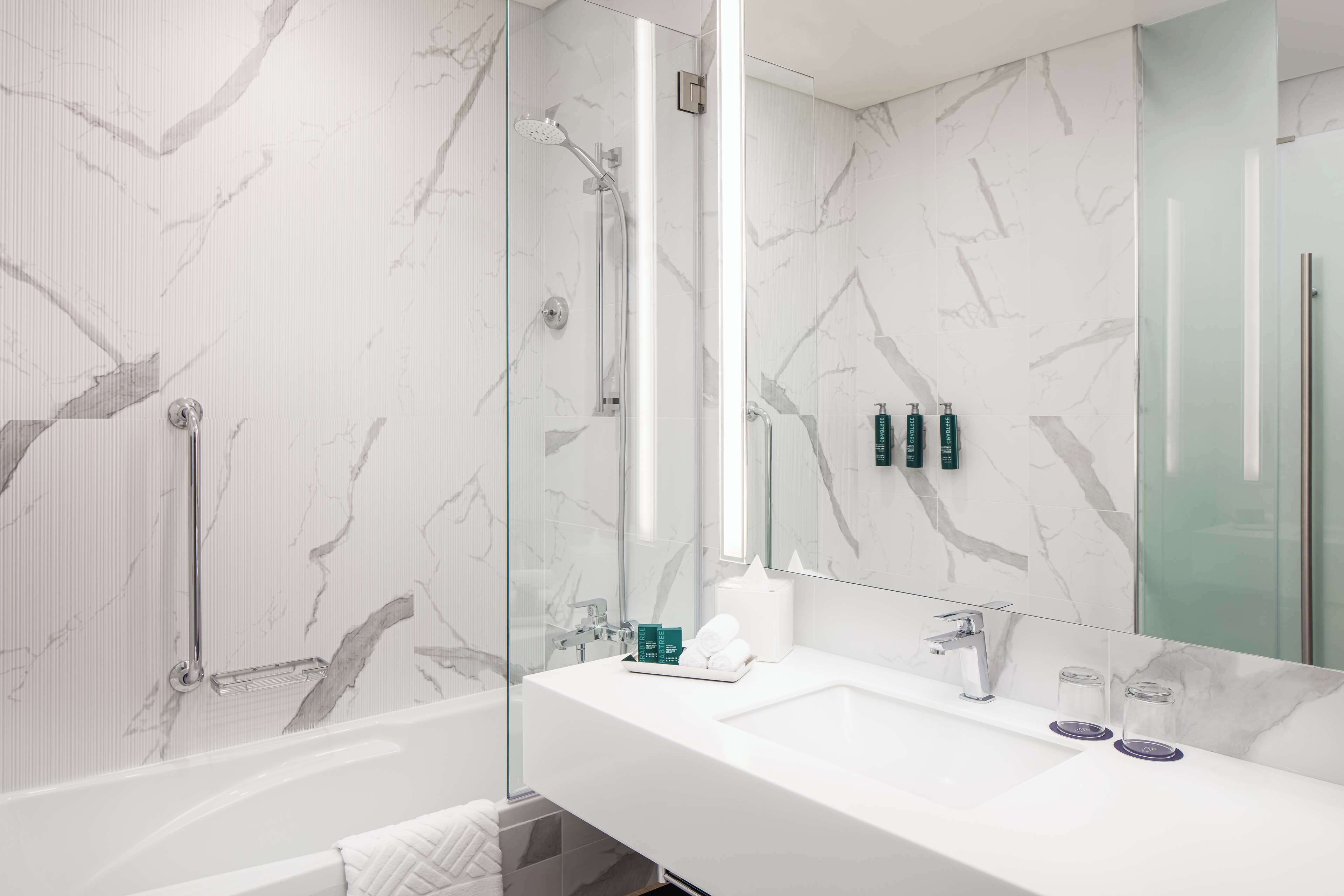 A modern bathroom with a glass-enclosed shower, a white sink with two soap dispensers, and a large mirror.
