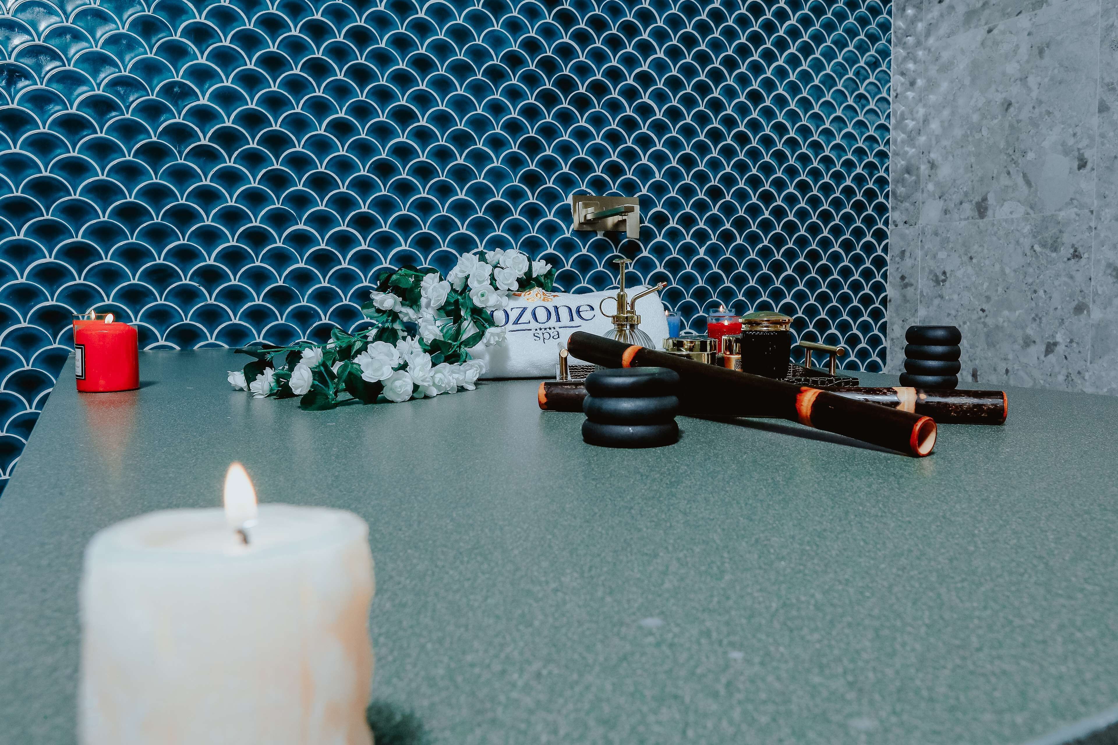 Una habitación con pared azul estampada, una vela blanca, una planta pequeña y un objeto decorativo sobre la mesa.