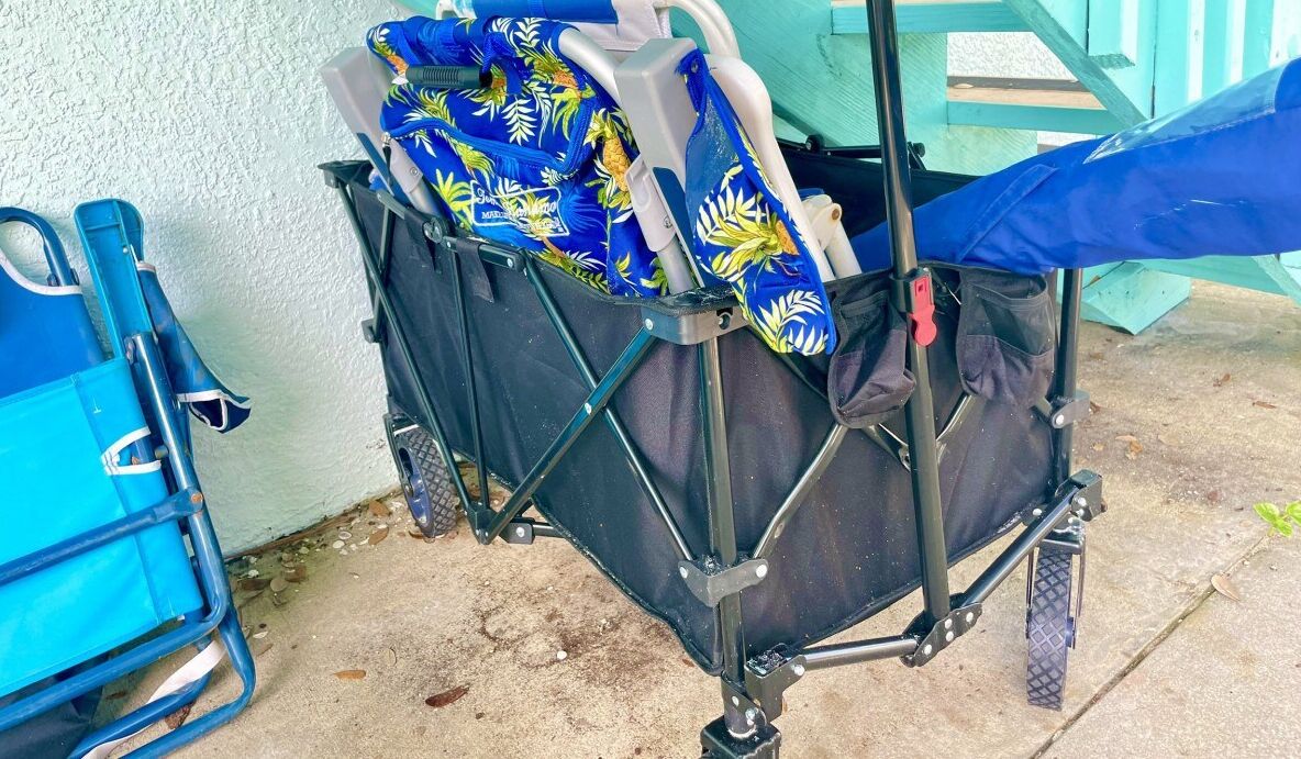 A black luggage cart with a blue umbrella and a blue chair beside it.