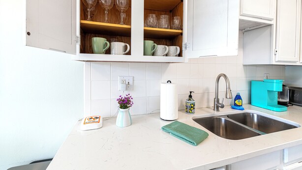 A kitchen with white cabinets, a sink, a coffee maker, and a vase with flowers on the counter. - Cozy 2-bed, 1-bath second-floor unit minutes from Indian Rocks Beach. Sleeps 7 with full kitchen, WiFi, smart TV, beach gear, parking, and direct pool access. A bright, comfortable stay for families and groups (Indian Rocks Beach)