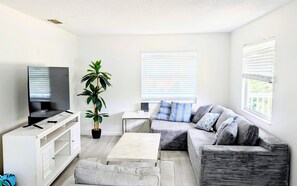 A modern living room with a flat-screen TV, a potted plant, a sofa with patterned cushions, and a coffee table. - RENOVATED! Spacious 2-bed, 2-bath second-floor unit minutes from Indian Rocks Beach. Sleeps nine with full kitchen, WiFi, smart TV, beach gear, parking, and direct pool access. A comfortable, convenient stay for families and groups (Indian Rocks Beach)