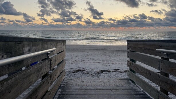 Una passerella di legno che conduce a una spiaggia con un tramonto sullo sfondo.
