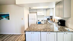 A compact kitchen with white cabinets, a granite countertop, and basic appliances including a refrigerator, microwave, and stove. - Spacious 2-bed, 2-bath second-floor unit near Indian Rocks Beach. Sleeps eight with full kitchen, WiFi, smart TV, shared pool access, and beach gear. A bright, comfortable base for families and groups looking for easy sand days and sunset evenings. (Indian Rocks Beach)