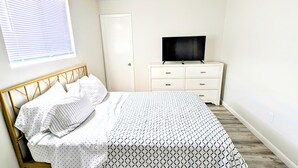 A bedroom with a bed, a dresser, a television, and a window with blinds. - Spacious 2-bed, 2-bath second-floor unit near Indian Rocks Beach. Sleeps eight with full kitchen, WiFi, smart TV, shared pool access, and beach gear. A bright, comfortable base for families and groups looking for easy sand days and sunset evenings. (Indian Rocks Beach)