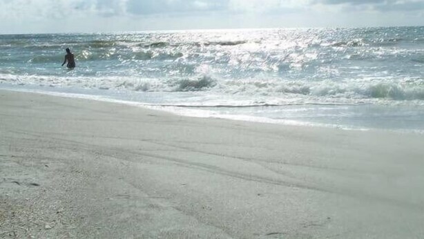 A beach with waves and a person in the water.