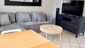 A living room with a sofa, a TV, a ceiling fan, a dining table, and a small round table.