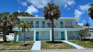 A two-story building with a light blue exterior, numbered rooms, and a balcony on the upper floor.