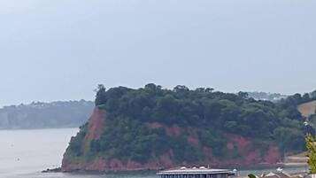 A coastal town with buildings near the water, a prominent red cliff, and a large building with a flat roof.