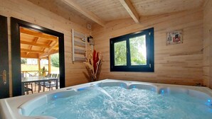 Een houten hut met een hottub, een eethoek en een raam met uitzicht op groen.