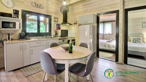 Een gezellige, goed verlichte keuken met moderne apparatuur, een eethoek met een tafel en stoelen, en een slaapkamer met een bed en gordijnen.