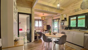 Een gezellig interieur met een houten eettafel, stoelen, een keukenhoek en een zithoek met een bank en televisie.
