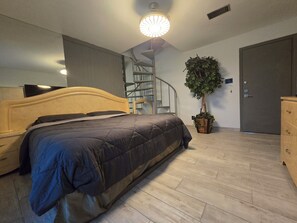 A bedroom with a bed, a dresser, a potted plant, a staircase, and a door. - Urban Treehouse (Dallas)
