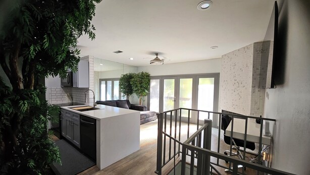 A modern kitchen with a central island, a dining area with a view, and a staircase leading to an upper level. - Urban Treehouse (Dallas)