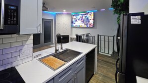 A modern kitchen with white cabinets, a stainless steel sink, a microwave, and a black refrigerator. - Urban Treehouse (Dallas)