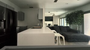 A modern kitchen with a central island, dark cabinetry, and a large window. - Urban Treehouse (Dallas)