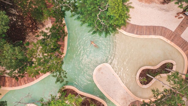 Vue aérienne d’un espace paysager agrémenté d’un cours d’eau sinueux, entouré d’arbres et d’une terrasse en bois.
