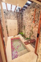 Un área de spa con una pared de piedra, un banco de madera y una bañera llena de agua y pétalos de rosa.