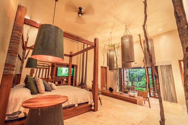 A spacious bedroom with a large bed, a wooden headboard, a television, and a view of the outdoors.