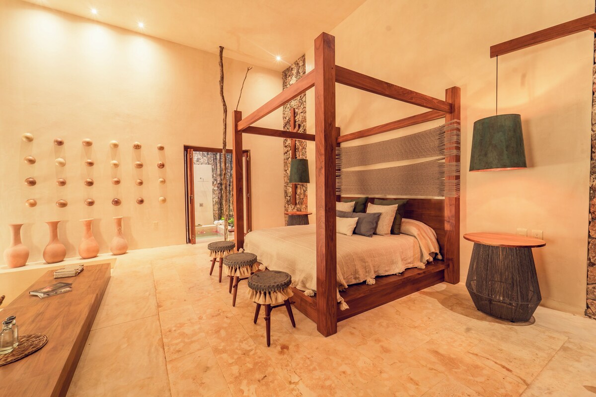 A four-poster bed with a wooden frame, a round table, and a wall-mounted vase collection.