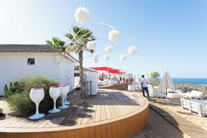 A wooden deck with white wine glasses, a palm tree, and a beach in the background.
