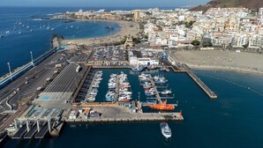 An aerial view of a marina with boats docked, a parking area, and a beach in the background. - Home2Book Beachfront Design&Views Los Cristianos (Los Cristianos)