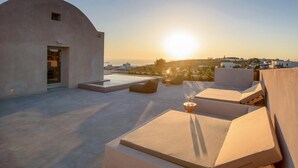 Una terraza en la azotea con un muro curvo, zonas de estar y vistas al atardecer sobre un paisaje costero.