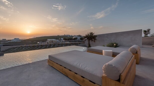 A rooftop terrace with a view of the sunset over the sea, featuring two wooden beds and a small pool.