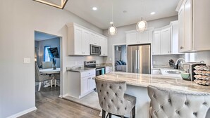 Una cocina moderna con armarios blancos, una isla de mármol y un refrigerador de acero inoxidable.