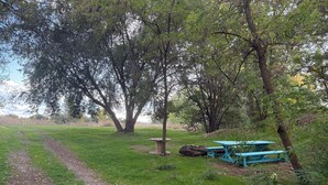 A picnic area with a dirt path, a wooden bench, and a picnic table in a grassy field surrounded by trees. - Wonderful campground in Caldwell with stunning views. And a shared private lake. (Caldwell)
