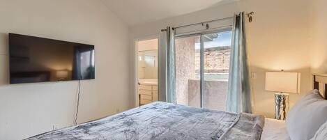 Una camera d'albergo con un letto, una TV a muro, una finestra con tende e vista sull'esterno.