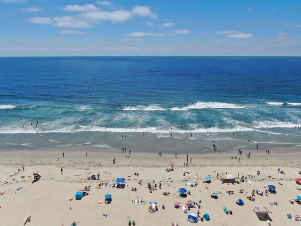 A beach with people sunbathing and swimming, and a clear view of the ocean.