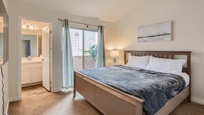 A bedroom with a bed, a nightstand, a window with curtains, and a bathroom visible through an open door. - 1 Block to Pacific Beach/FOOD/Bars, Updated, 2-Car Garage w/fee, Yard, Sleeps 12 (San Diego)