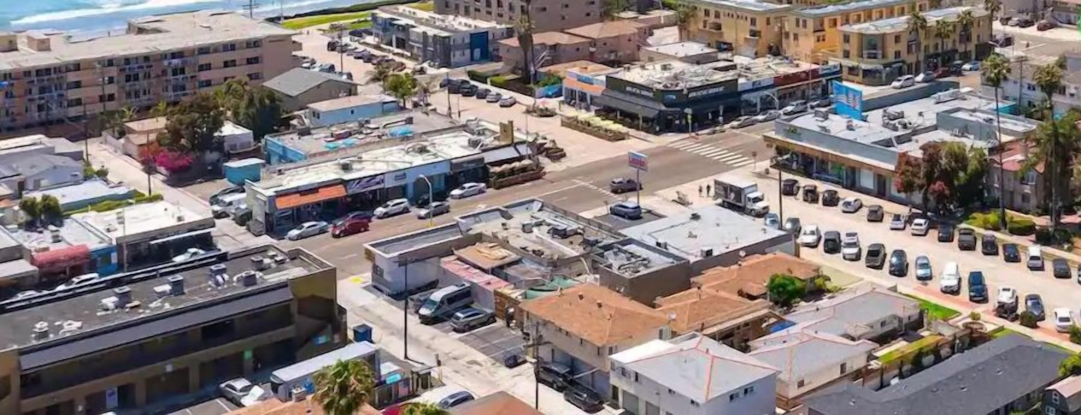 Vue aérienne d’une zone commerciale comprenant plusieurs bâtiments, des parkings et un carrefour.