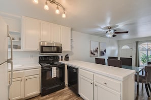 A modern kitchen with white cabinetry, a black stove, a microwave, and a ceiling fan.