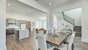 A spacious kitchen with a central island, a dining area with a large wooden table and chairs, and a staircase leading to an upper level. - Luxurious & Spacious Austin Home ~ 8 Mi to Dtwn! (Austin)