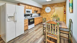 A compact kitchen with wooden cabinets, a white refrigerator, a microwave, and a stove. There's a dining table with chairs and a clock on the wall. - Mountain Retreat < 4 Mi to Downtown Boone! (Boone)