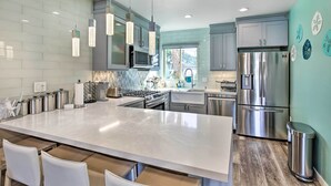 Una cucina moderna con un'isola grande, elettrodomestici in acciaio inossidabile e illuminazione a sospensione.