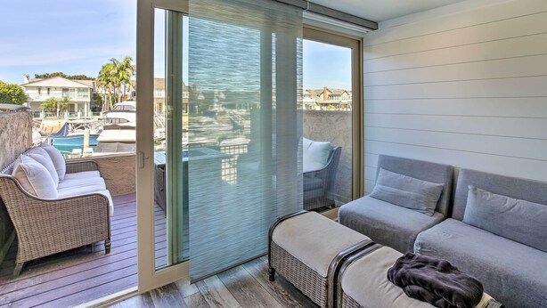 Un balcone con un divano in vimini, un divano grigio e una porta vetrata che dà su un'area piscina.