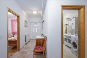 A narrow hallway with a wooden chair, a bed, a radiator, a washing machine, and a bathroom with a sink and mirror. - Villa Vera Apt 1 - in House with Pool (Banjole)