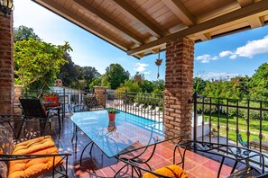 A covered patio with a glass table and chairs, a brick wall, and a view of a swimming pool and garden. - Villa Vera Apt 1 - in House with Pool (Banjole)